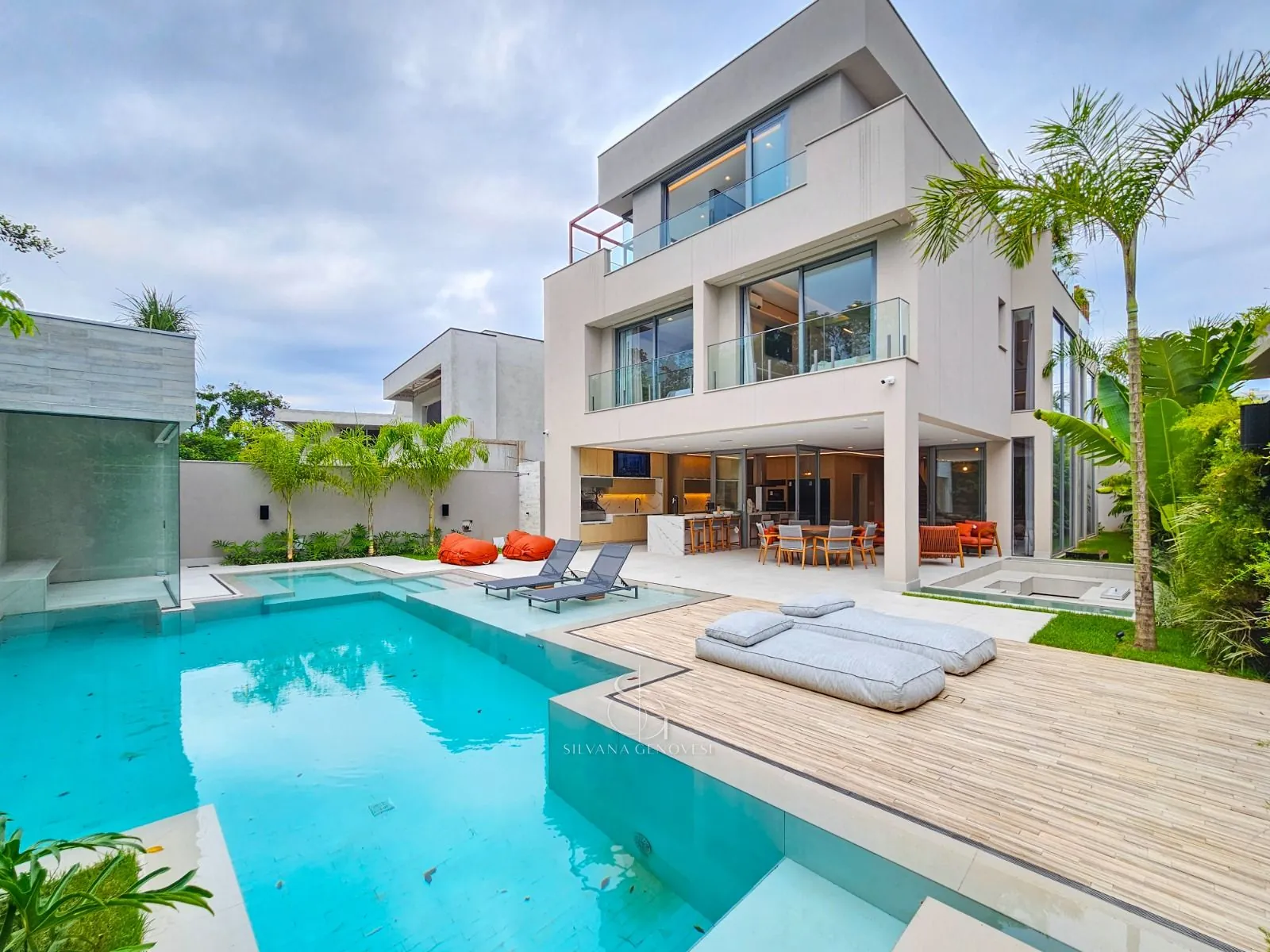 Fachada contemporânea de três pavimentos com piscina, deck de madeira e vegetação